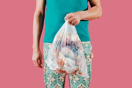 a man holding a trash bag with food waste against pink