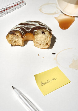 Doughnut and Deadline Note on Desk With Coffee Stains and Pen