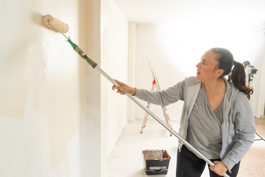 Woman renovating home painting interior wall with roller