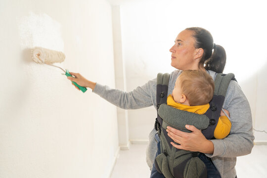 Mother renovating home painting wall with baby carrier