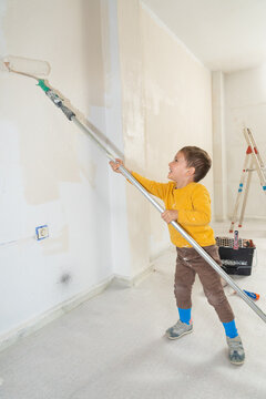 Boy helping painting wall with roller during home renovation