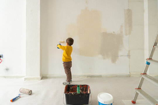 Little boy helping painting home wall with roller