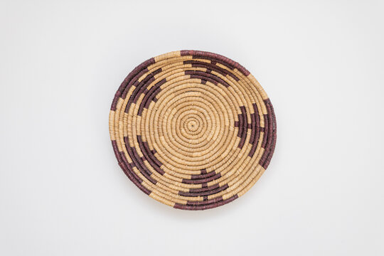 Handcrafted circular woven bowl featuring intricate geometric designs in dark purple and natural straw fibers, shown from a top-down perspective on a clean white background for versatile design