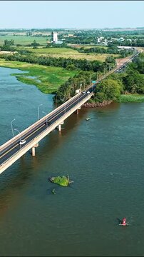 Aerial drone flyover over long highway bridge above river approaching city with vehicles, vertical video 9:16