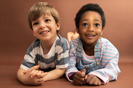 Diverse children smiling, lying on brown background
