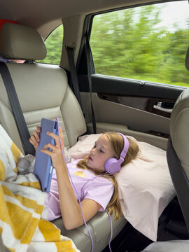Young girl listen music headphones in car with tablet 