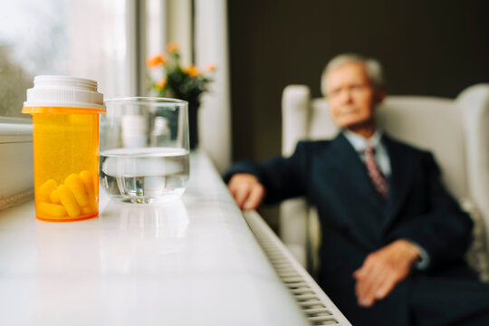 Medicine on the window sill, senior man sitting at the background