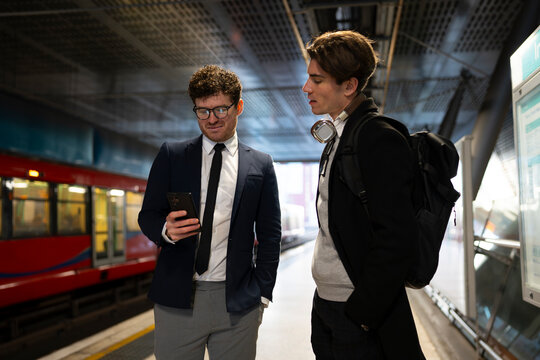 Two men wait at train station
