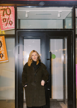 Woman Standing in Front of Store With Sale Signs in City at Night