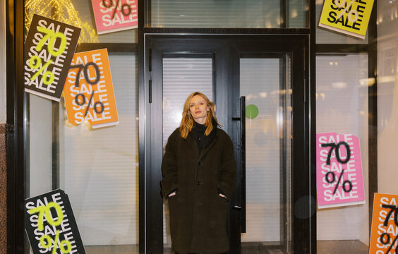Woman Stands in Front of Sale Signs at a Closed Store in the City