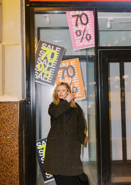 Woman Stands Near Shop Window With Sale Signs in City Center