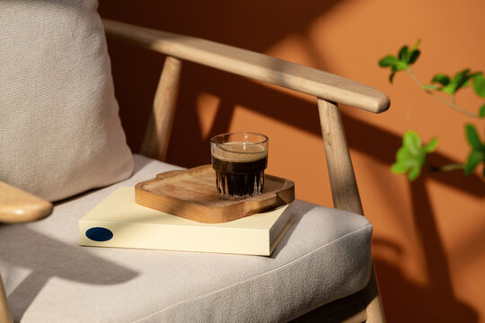 Coffee in a glass on a wooden tray with a book on a chair
