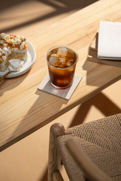 Iced coffee with ice cubes on a wooden table with a slice of cake