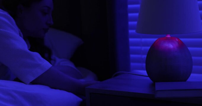 Woman putting book onto nightstand, turning off night lamp and lying down for sleep in bed at home, closeup