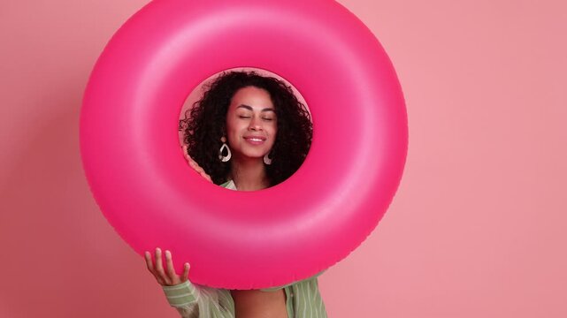 Beautiful woman in beachwear with inflatable ring on pink background