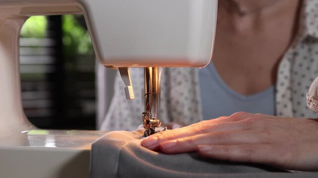 Woman sewing fabric with professional machine in workshop, closeup
