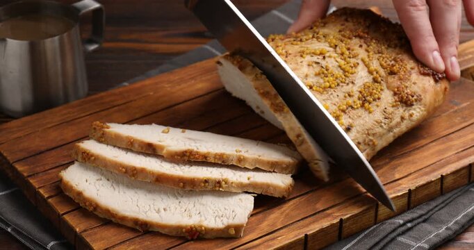 Woman cutting tasty baked turkey with knife at wooden table, closeup