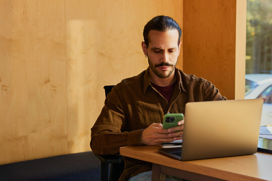 Man checking smartphone while working on laptop at desk