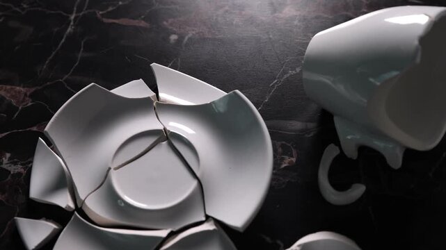 Pieces of broken saucer and cup on black table, closeup. Camera moving forward