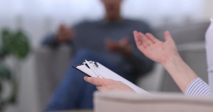 Professional psychologist making notes on clipboard during therapy session with patient indoors, selective focus