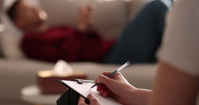 Professional psychologist making notes on clipboard during therapy session with patient indoors, selective focus