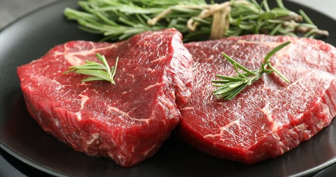 Raw beef steaks and rosemary on table, closeup