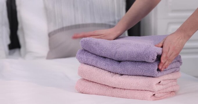 Woman with stack of soft towels on bed indoors, closeup