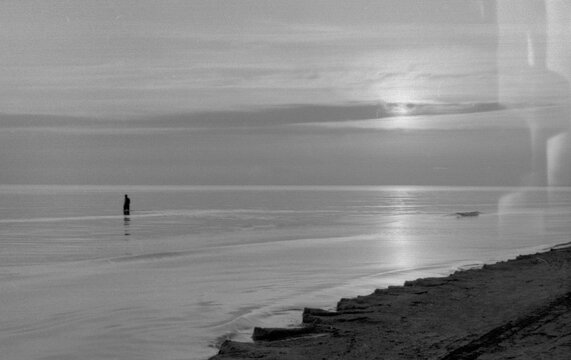 Person Alone Stands in Shallow Water at Sunset by the Beach