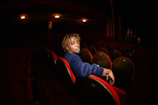 Person sits alone in red theater chairs during a show