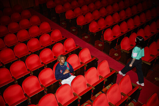 Person sitting in red seats in theater while another walks by