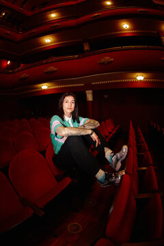 Person sitting in a theater with red seats during a performance