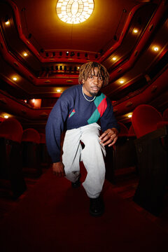 Man kneeling in theater with empty red chairs and bright ceiling