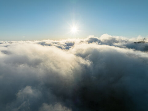 Aerial view of a thick layer of white clouds under a bright sun and clear blue sky in Madeira, Portugal.