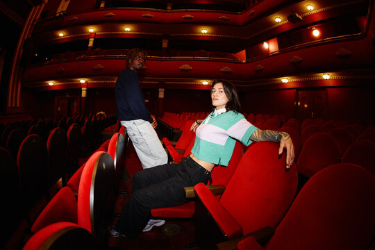 Two people sitting in red theater seats at an empty venue