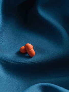 Two orange pills are neatly arranged on rippled, dark blue