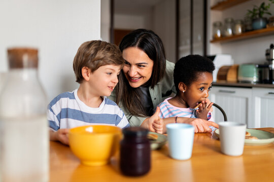 Happy mother teaching diverse children cooking pancakes
