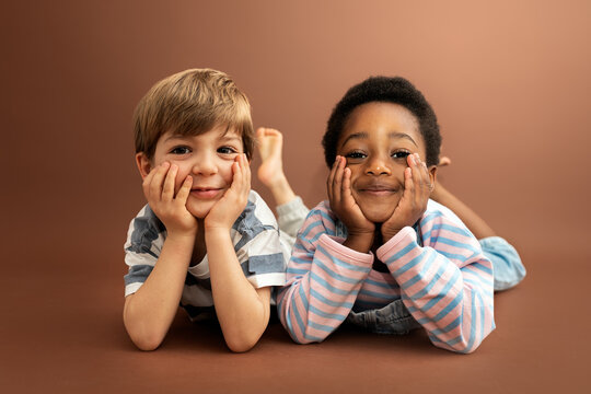 Diverse children smiling, lying on brown background
