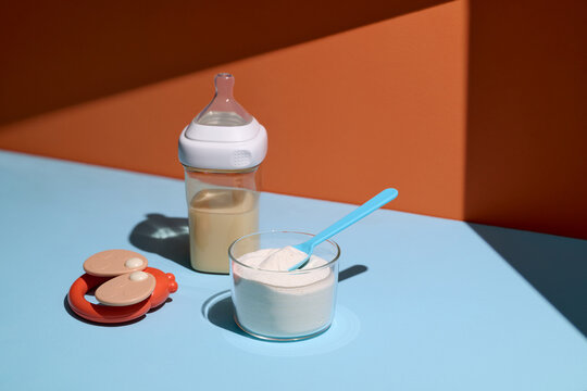 Baby bottle with milk, powdered formula, and a rattle on a table