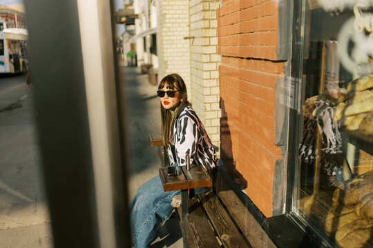 Woman Sitting on Bench Outside Store During Sunny Day