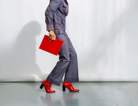 Person Walks in Denim Outfit With Red Shoes in Studio Setting
