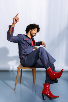 Man in Stylish Outfit Sitting on Chair With One Hand Raised