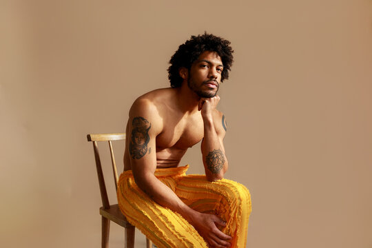 Man in Yellow Pants Sits on Chair Against Beige Background