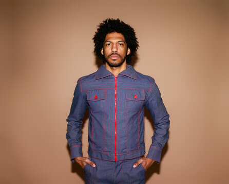 Stylish Man Wearing Denim Jacket Stands Against Plain Background