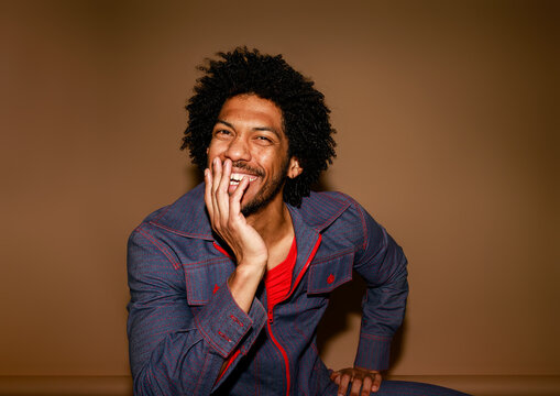 Smiling Man Poses in Stylish Outfit Against a Brown Background