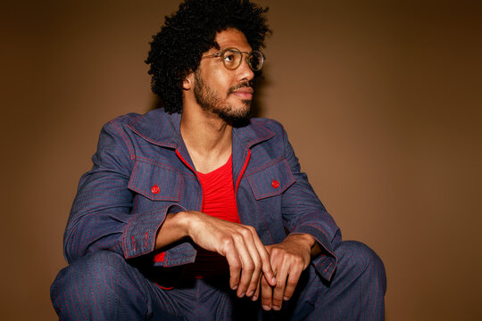 Man Sitting and Posing in Studio With Curly Hair and Glasses