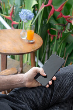Man Holding Smartphone with Blank Screen at Tropical Outdoor Cafe