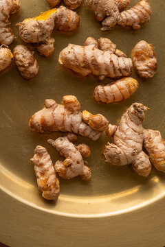 Turmeric Roots on a Golden Plate in Daylight With a Simple Background