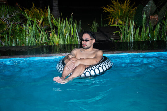 Man Relaxes in Pool on a Float Surrounded by Greenery at Night