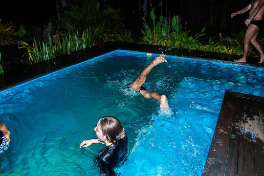 People Swimming and Playing in a Pool at Night in a tropical Setting