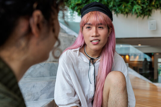 Pink-haired person in conversation, sitting on stairs.